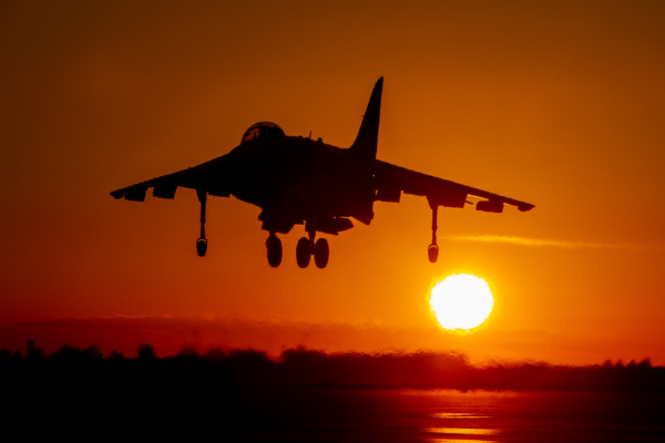 Fighter jet hovering over a runway with the setting sun in the background